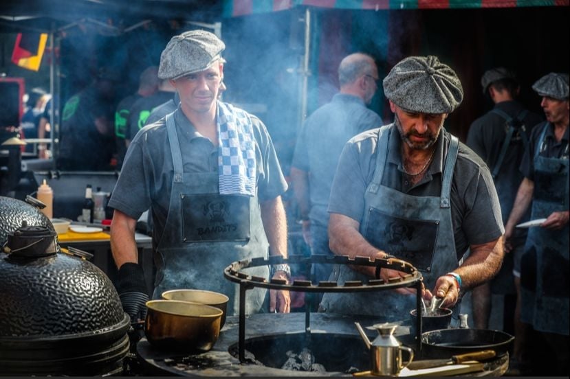 Male chefs in aprons and hats cooking over a large green egg grill with smoke