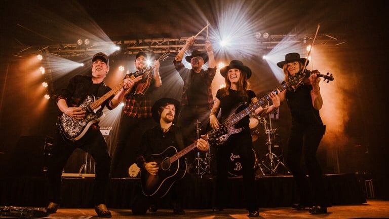 A live band performs on stage with warm lighting, featuring musicians playing guitar, bass, drums