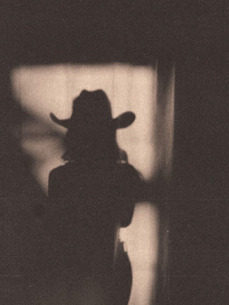 Silhouette of a person wearing a cowboy hat against a light rectangular background in a dark room