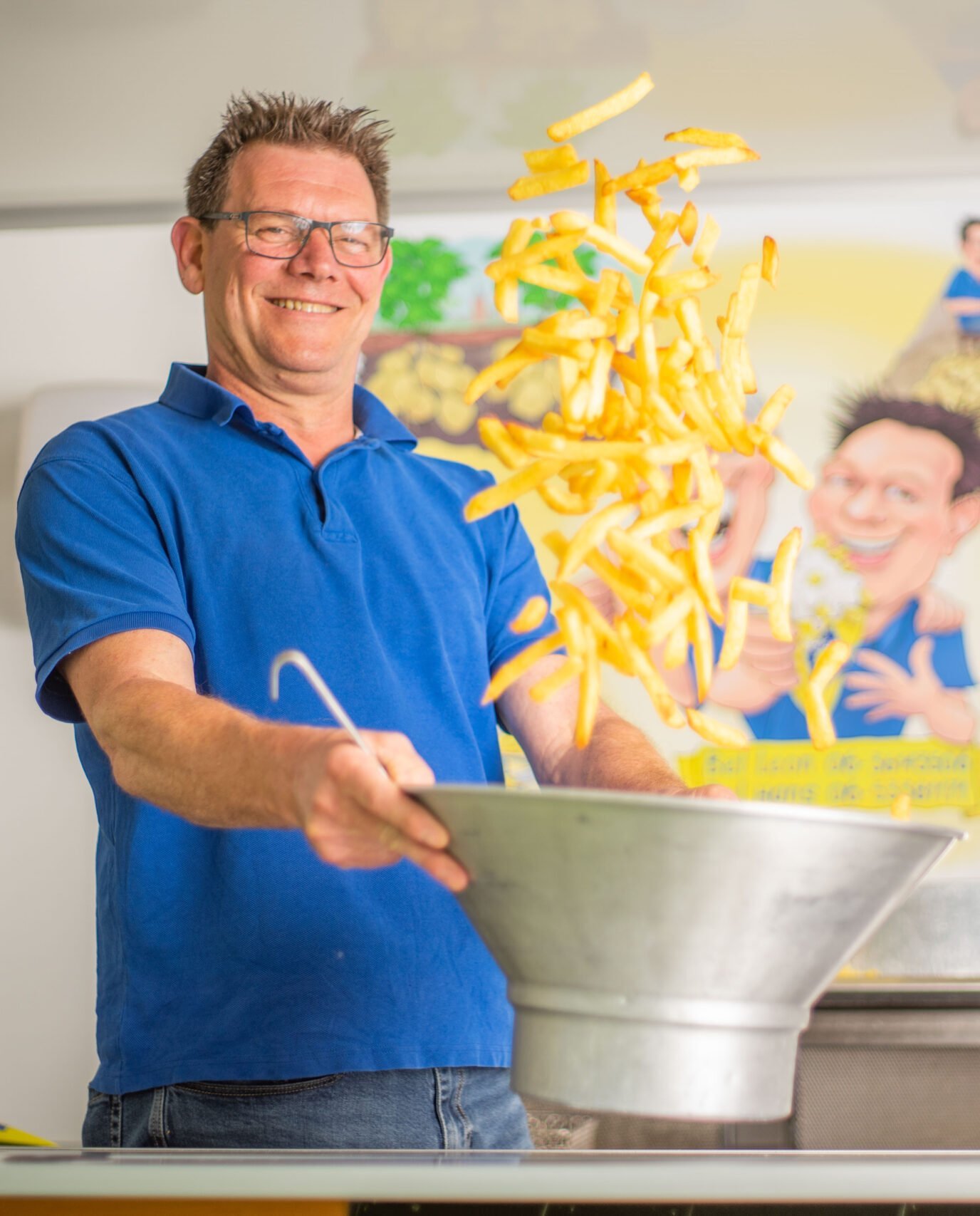 Man in blue polo shirt serving yellow noodles from a metal bowl during a cooking demonstration or event